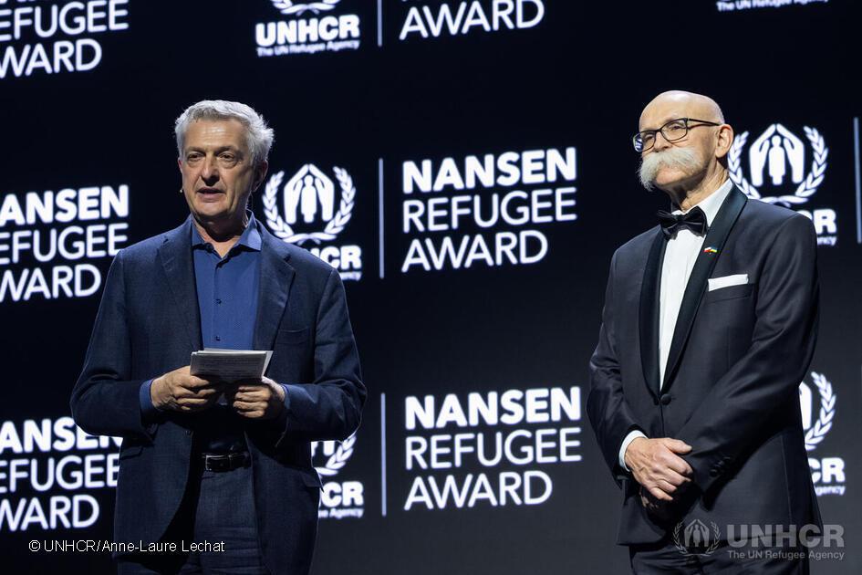 Dwie elegancko ubrane osoby na scenie, w tle ekran z napisem Nansen Refugee Award