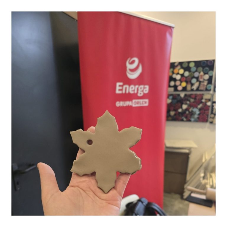 Trzymana w dłoni surowa, gliniana ozdoba w kształcie gwiazdki z otworem do zawieszenia. W tle baner Energa Grupa Orlen