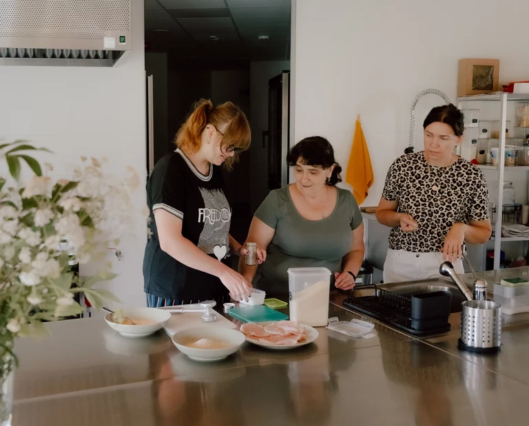 Trzy kobiety przygotowują posiłek w kuchni, pracując razem przy blacie kuchennym.